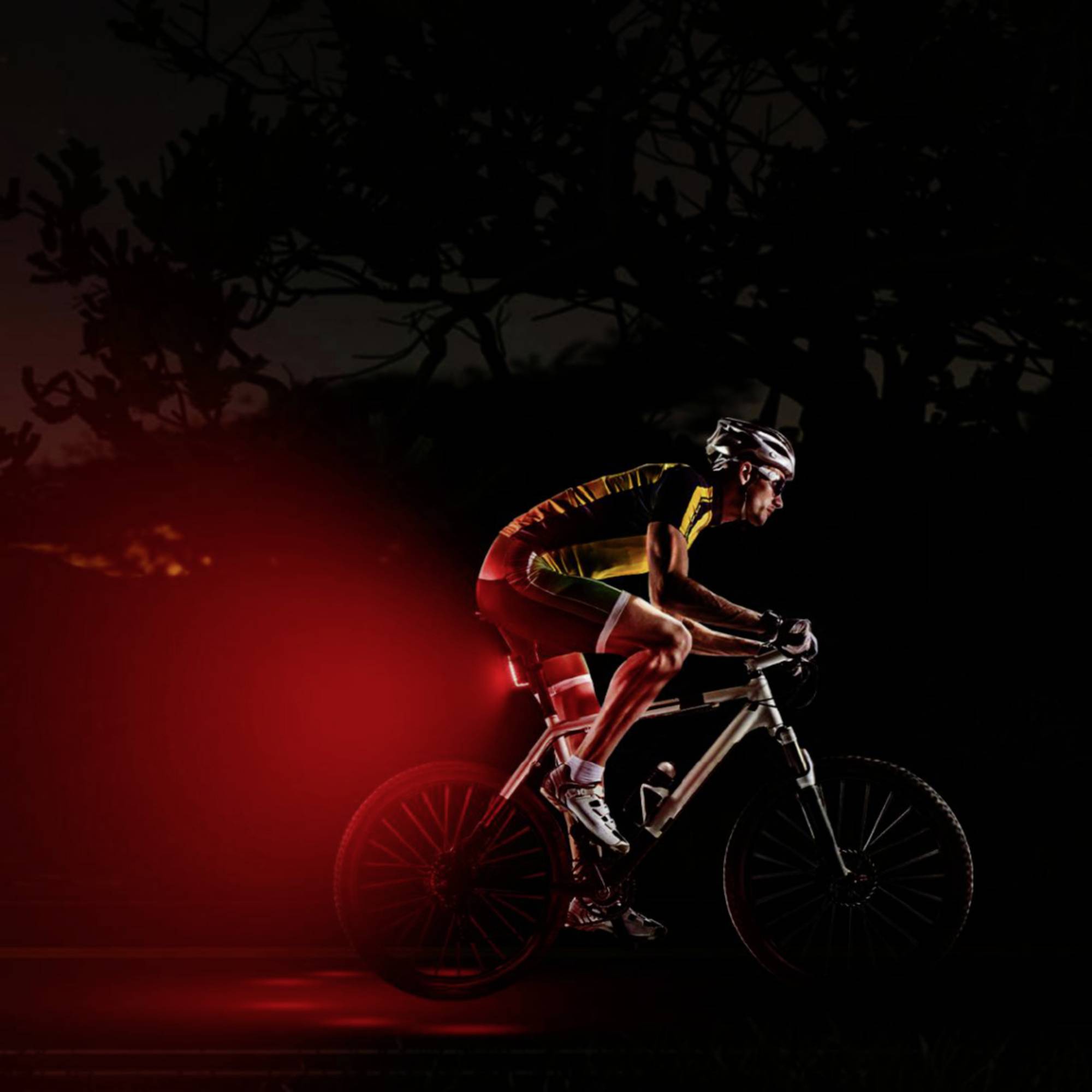 'Cyclist with a red rear light cycling at night on a dark road, wearing a helmet and cycling attire.'