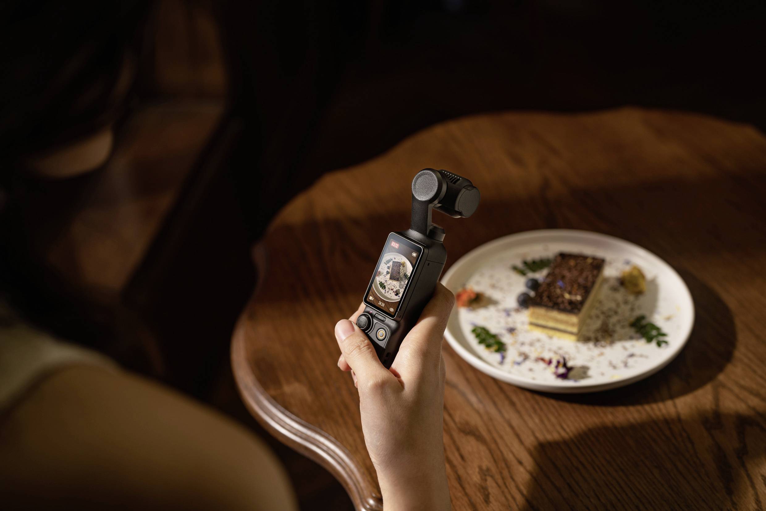 A person is photographing a dessert on a table using a small handheld camera. The dessert is artfully presented.