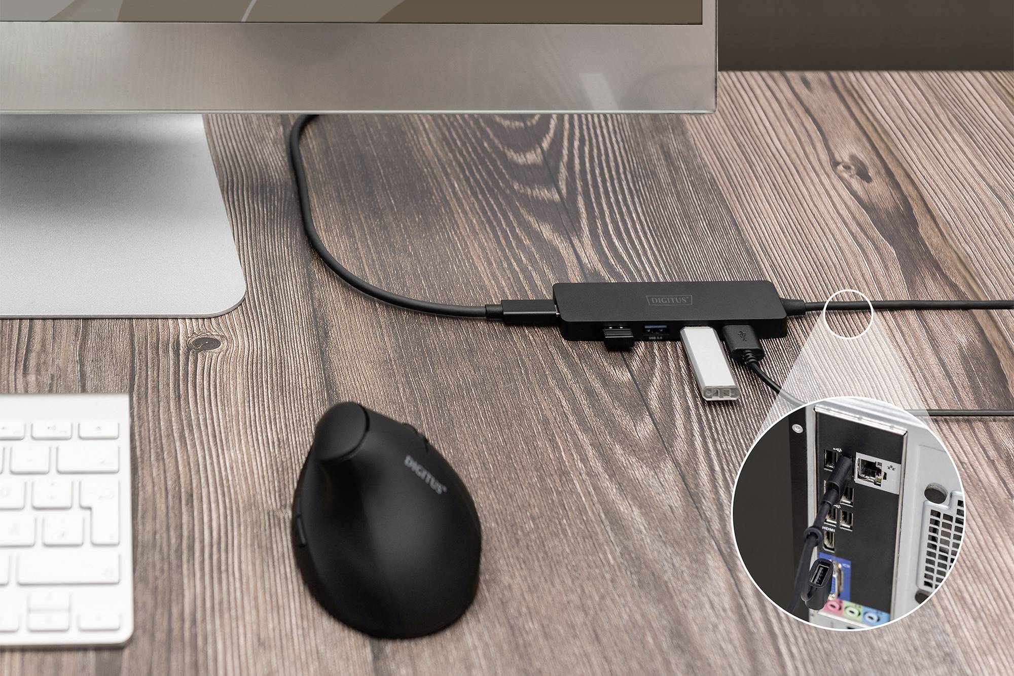 Monitor on a wooden table, USB hub with connected cable, circular cutout reveals PC back with network connection and USB ports.