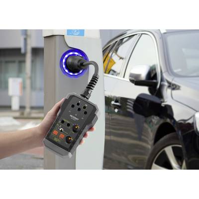 A hand is holding a measuring device connected to a charging station while a car is being charged.