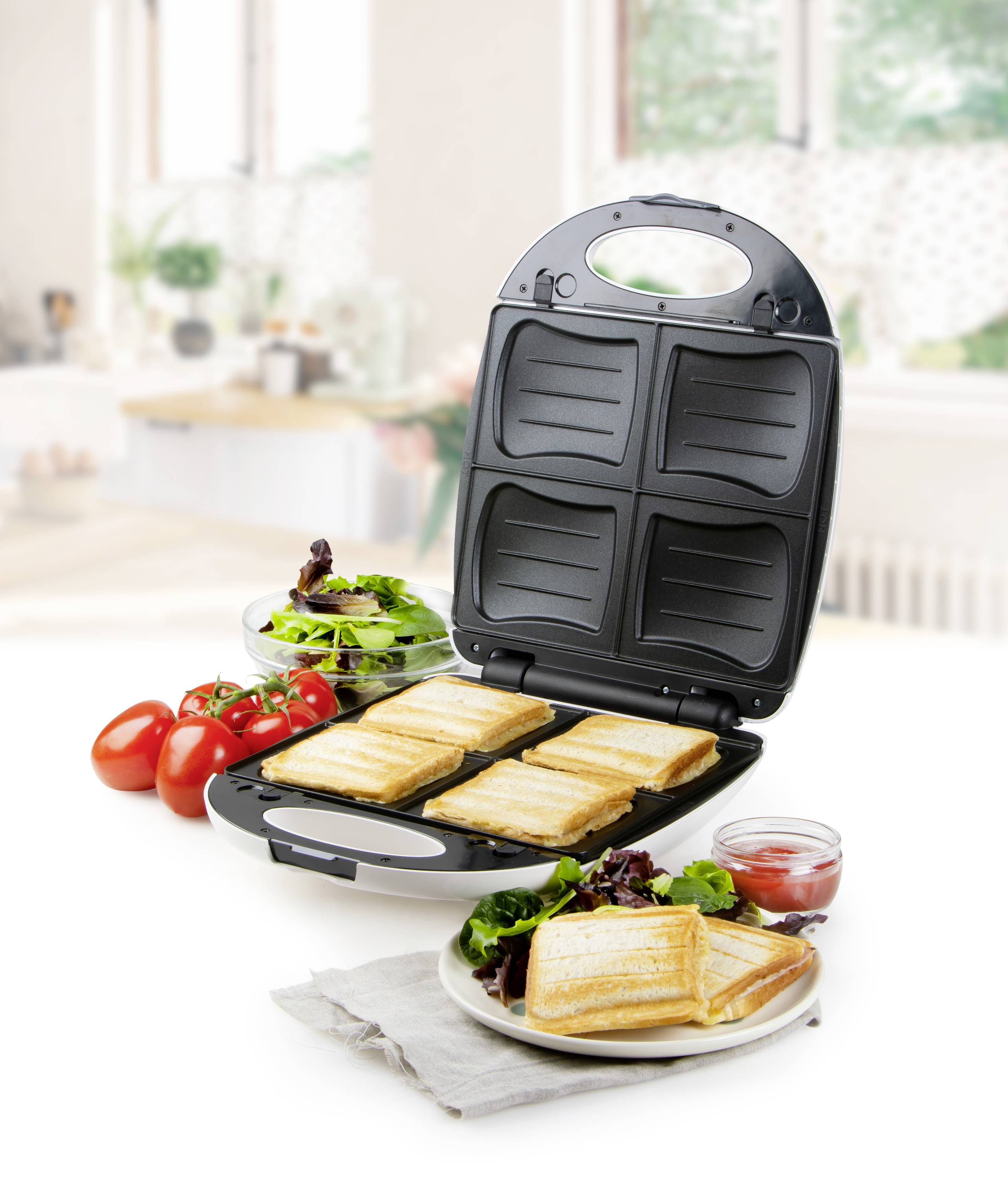A sandwich toaster on a kitchen worktop, toasting four sandwiches. Beside it are fresh tomatoes, a salad, and a jar of tomato sauce.