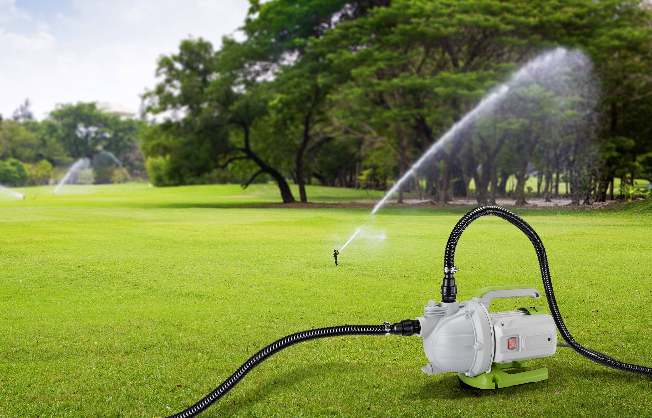A lawn pump with hoses in the foreground is irrigating a large, green lawn with several sprinkler systems in the background.