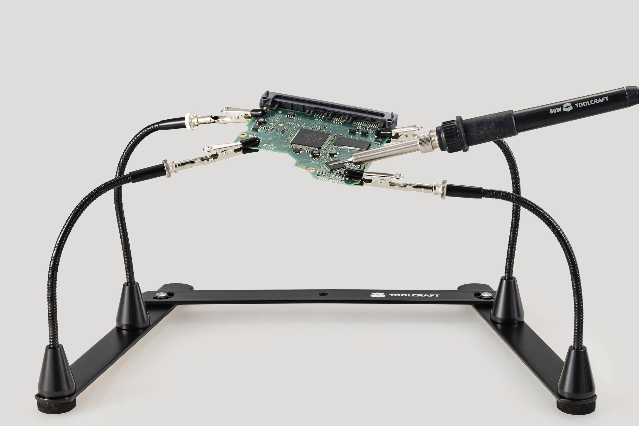 A soldering iron holds a circuit board on a flexible holder. The setup is suitable for safely soldering electronic components.