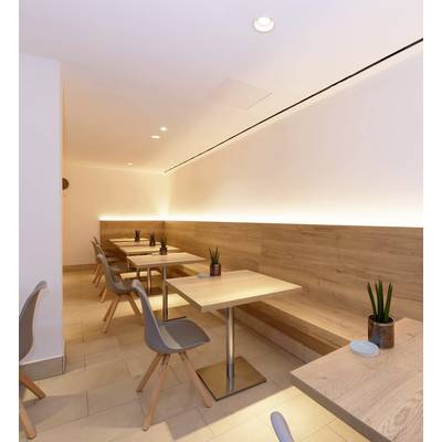 A modern, minimalist café area with wooden tables, grey chairs and subtle plant decoration in a bright setting.