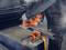 A person is working with an orange, portable metal saw to cut a square metal tube. Protective clothing is being worn.