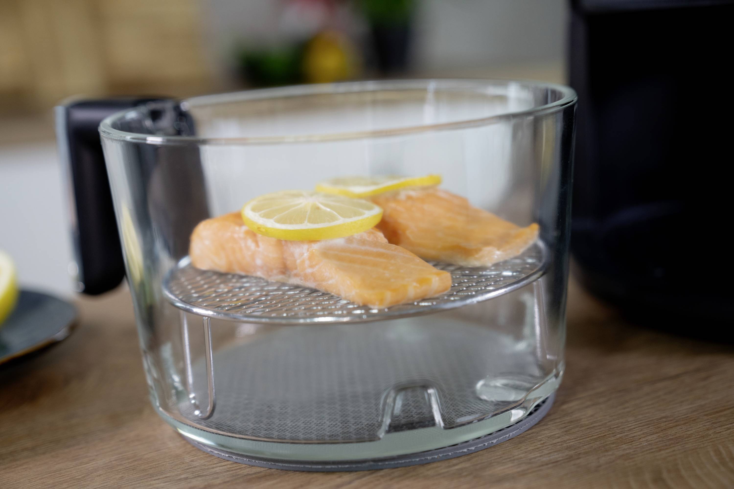 Two salmon fillets with lemon slices in a glass container, prepared for cooking.