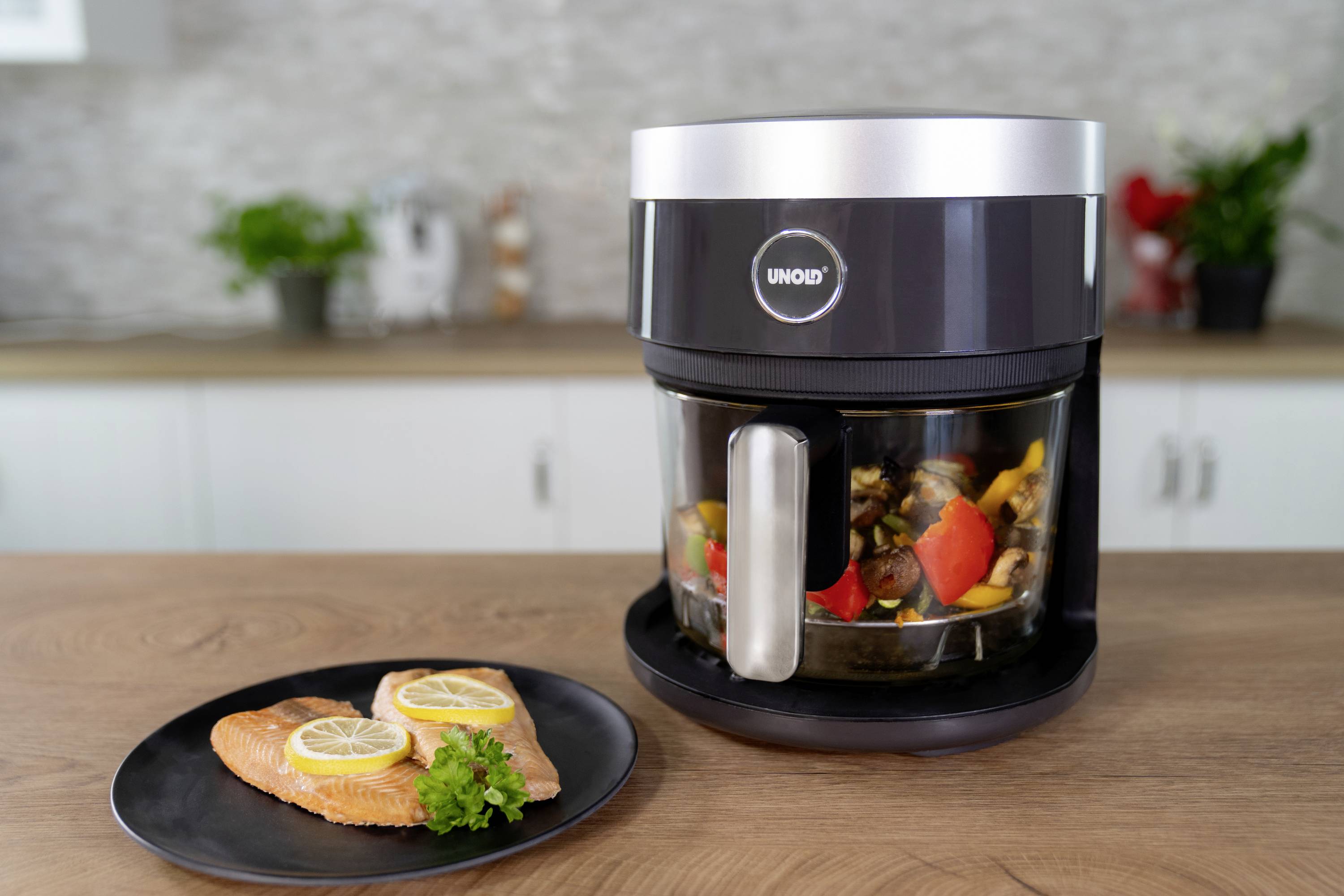 Air fryer with vegetables shows a healthy preparation method. In the foreground, a plate with salmon and lemon slices.