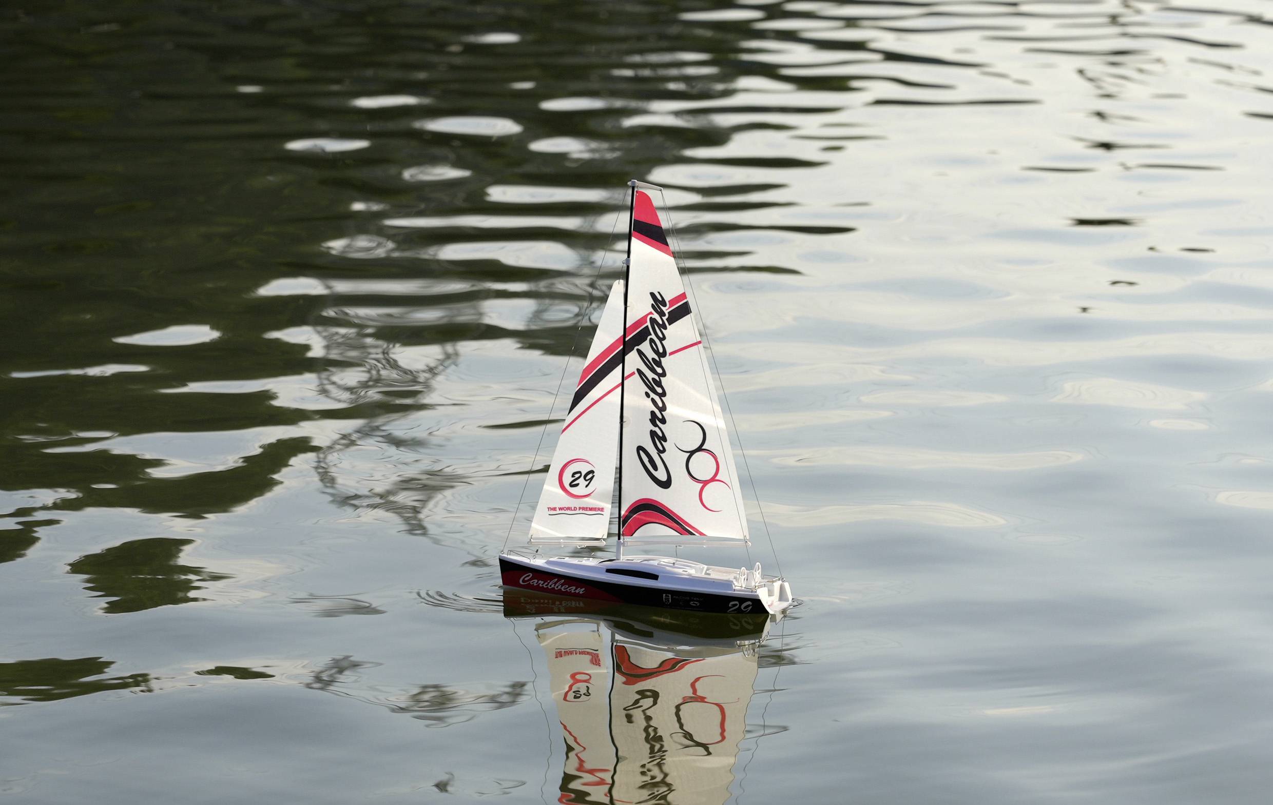 A small model sailing boat with the inscription 'Caribbean' sails on calm water.