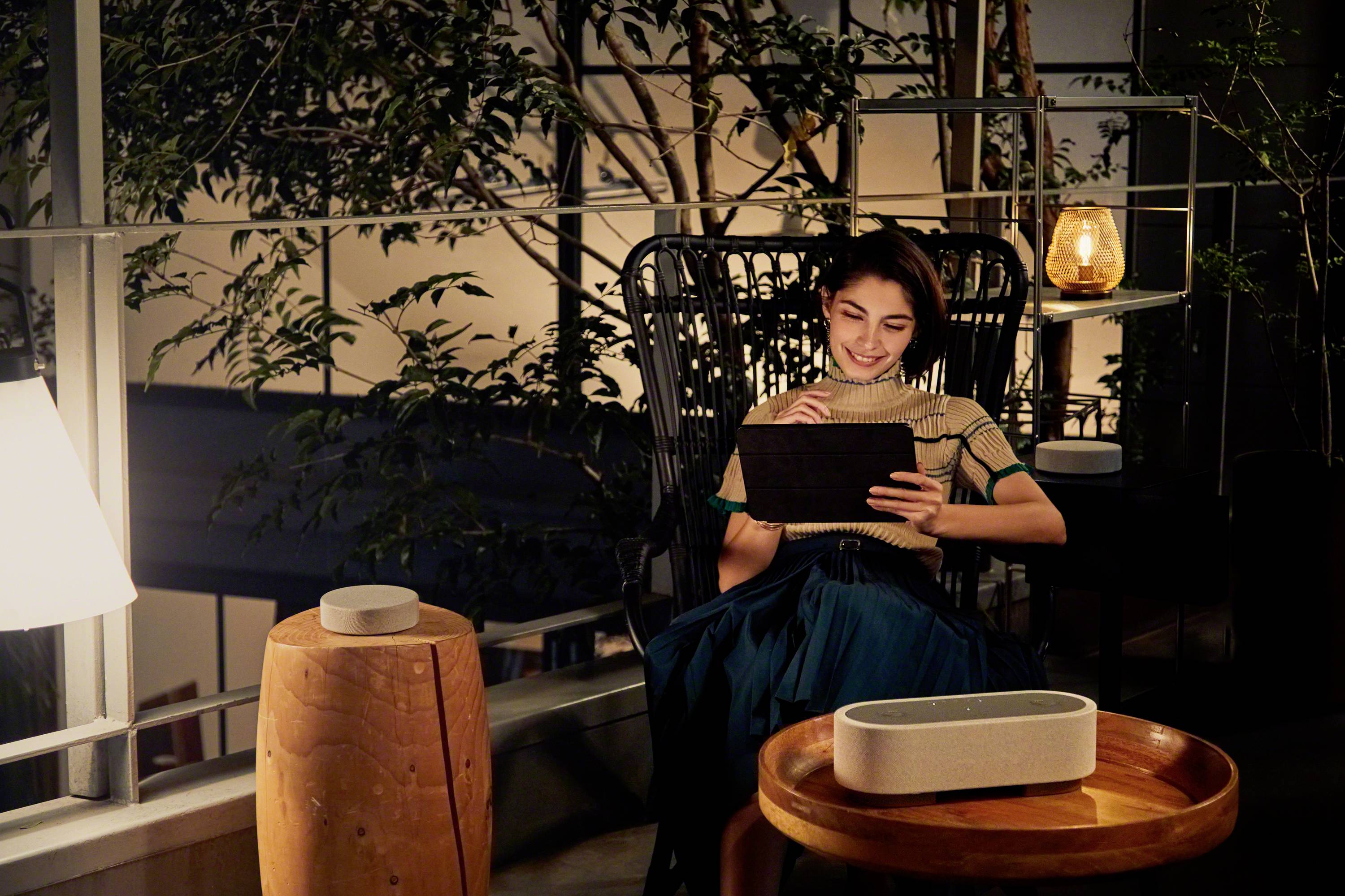 A person sits on a balcony in the evening, reading on a tablet, surrounded by plants and soft lighting.