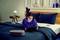 A woman is relaxing on a bed, smiling as she looks at a tablet. Smart speakers are positioned around her.