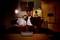 A couple sit cosily on a sofa in a room with atmospheric lighting. In front of them, a grey speaker sits on the table.