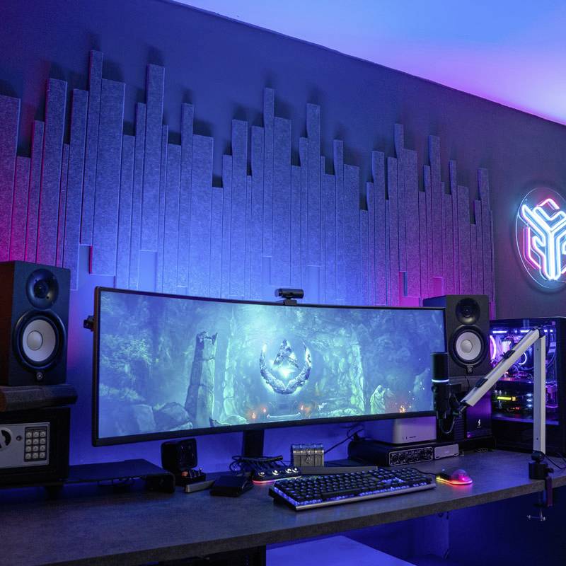 Gaming setup with an illuminated, curved monitor, surrounded by two speakers and a glowing computer tower on a desk.
