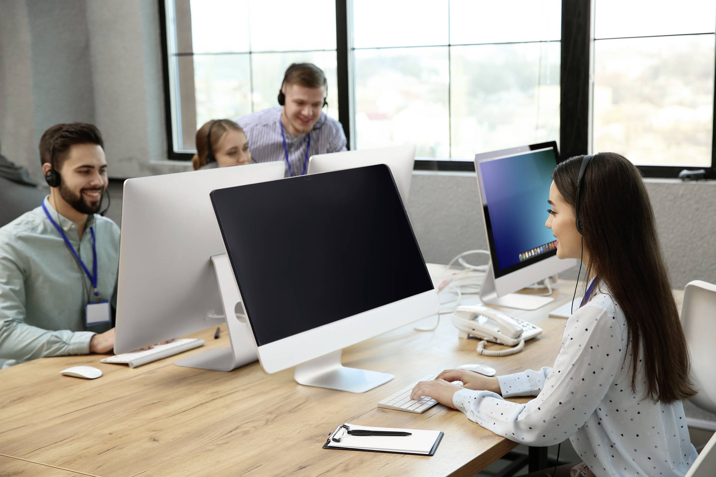 A group of people are working on computers in a modern office, looking focused and wearing headsets.