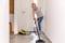 A woman is cleaning the floor in a corridor with a steam cleaner. She is wearing a light blue shirt and jeans.