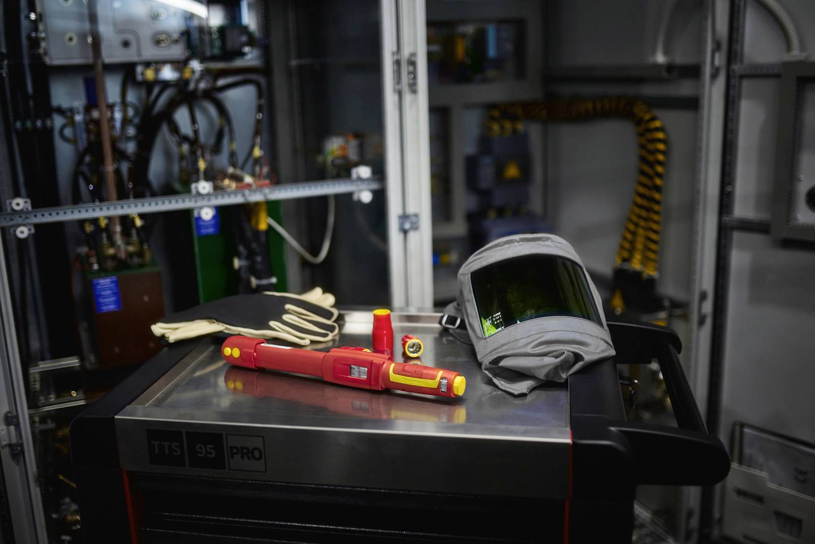 Safety helmet and tools are lying on a workshop trolley in front of an open electrical cabinet. This indicates electrical work is in progress.