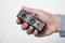 A hand is holding a small rectangular camera with multiple lenses and sensors. The camera is black and has a compact design.
