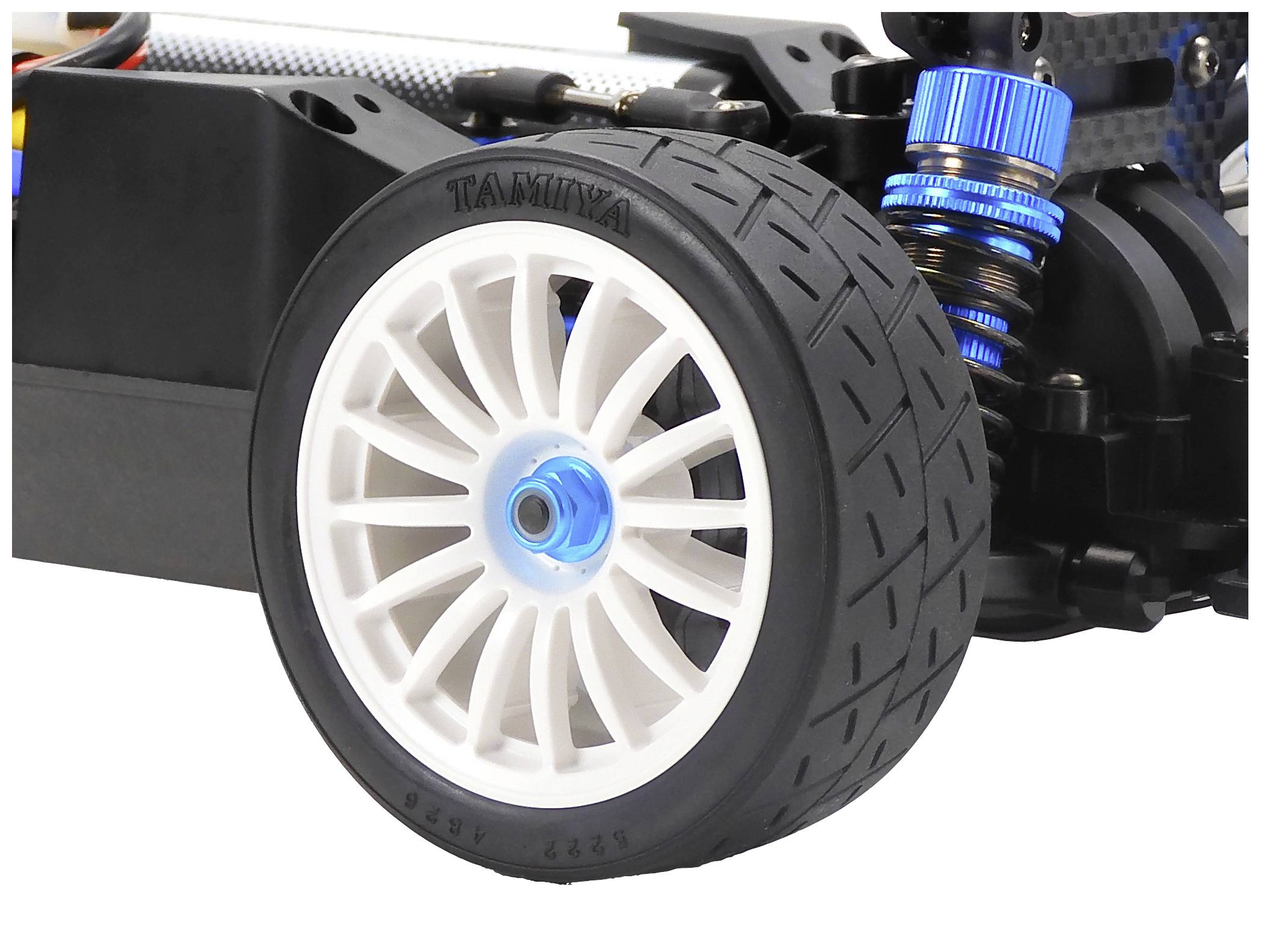 Part of a remote-controlled car with a detailed, white front wheel, blue suspension, and visible mechanical components.