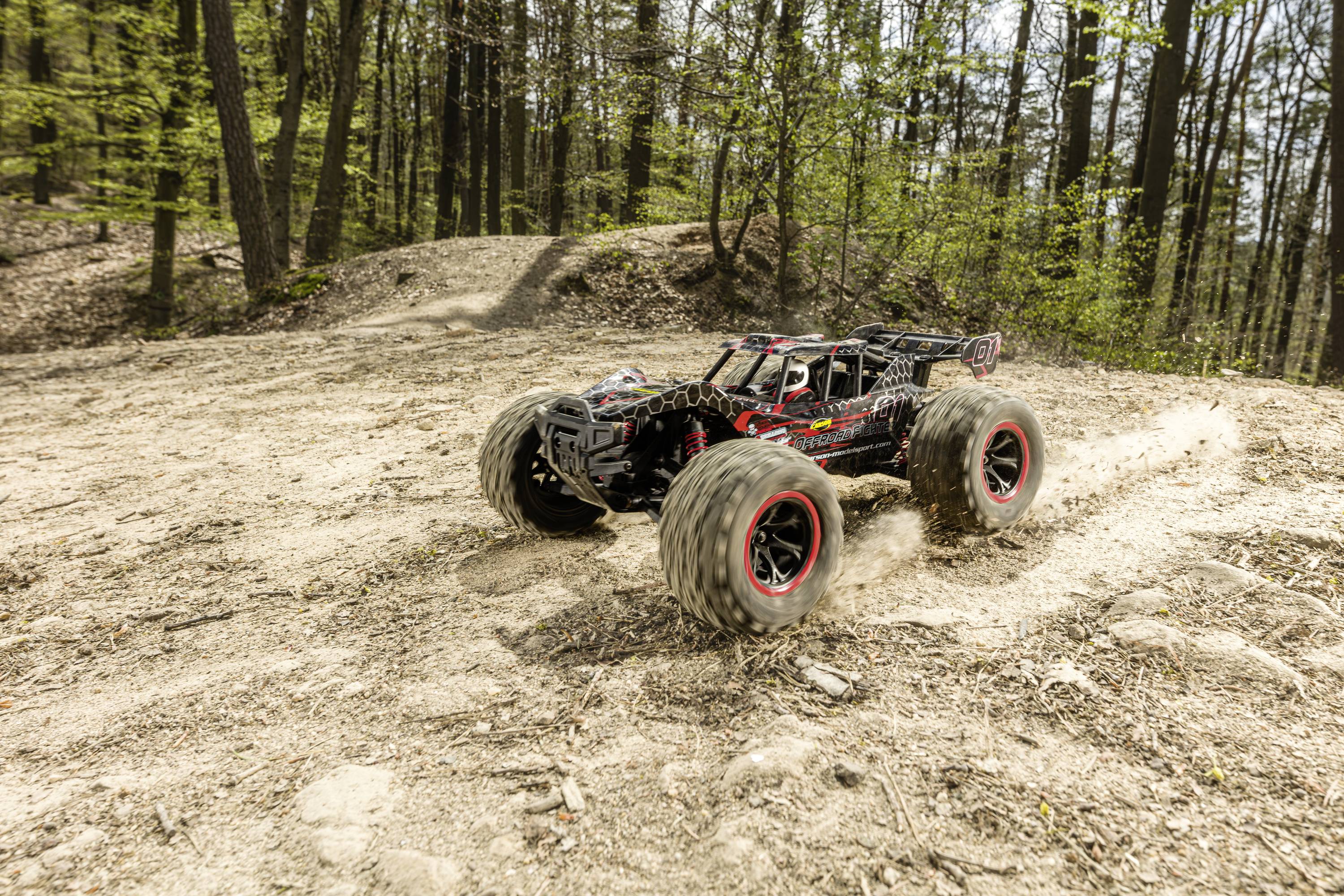 A remote-controlled car is driving at high speed along a bumpy forest track, kicking up dust from its wheels.