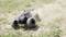 A remote-controlled car drives at high speed across a dusty, grass-covered terrain. Dust billows up behind the car.