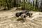 A remote-controlled car speeds along a sandy forest track. Large tyres kick up dust as the car drifts around a bend.