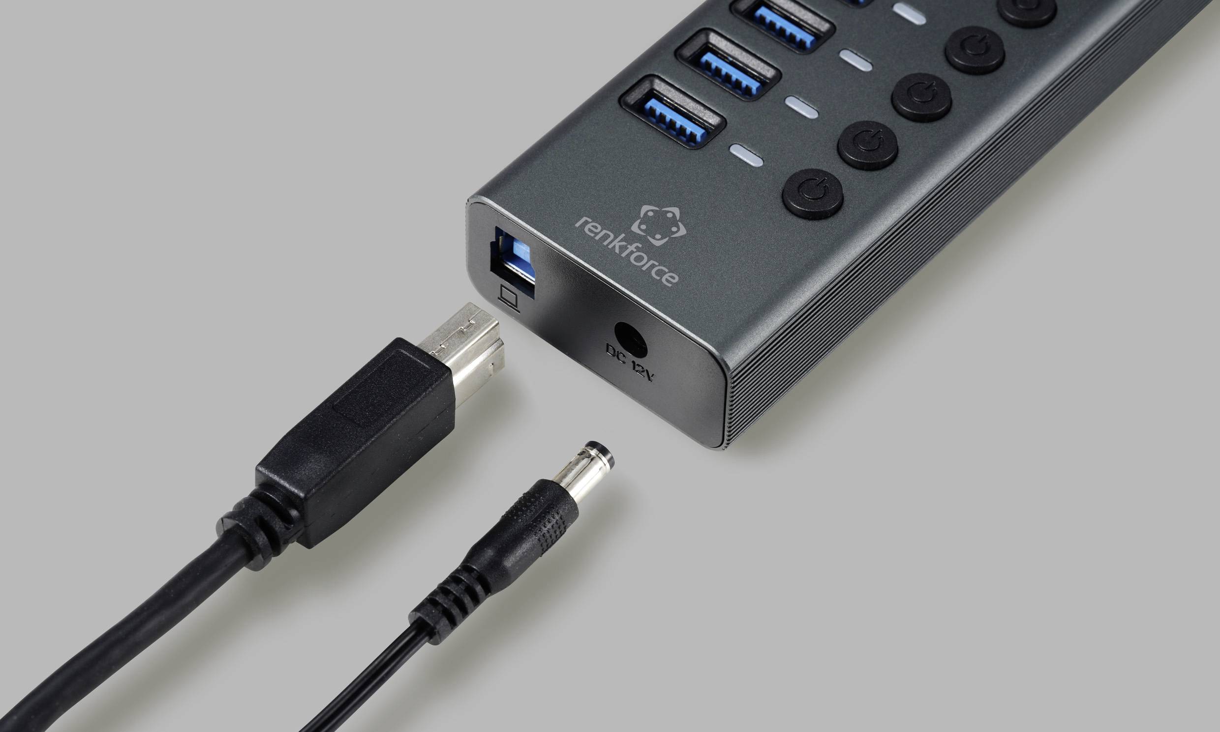 USB hub with four USB ports and on/off switches, 'renkforce' brand print, beside two cables, USB and power, on a grey background.