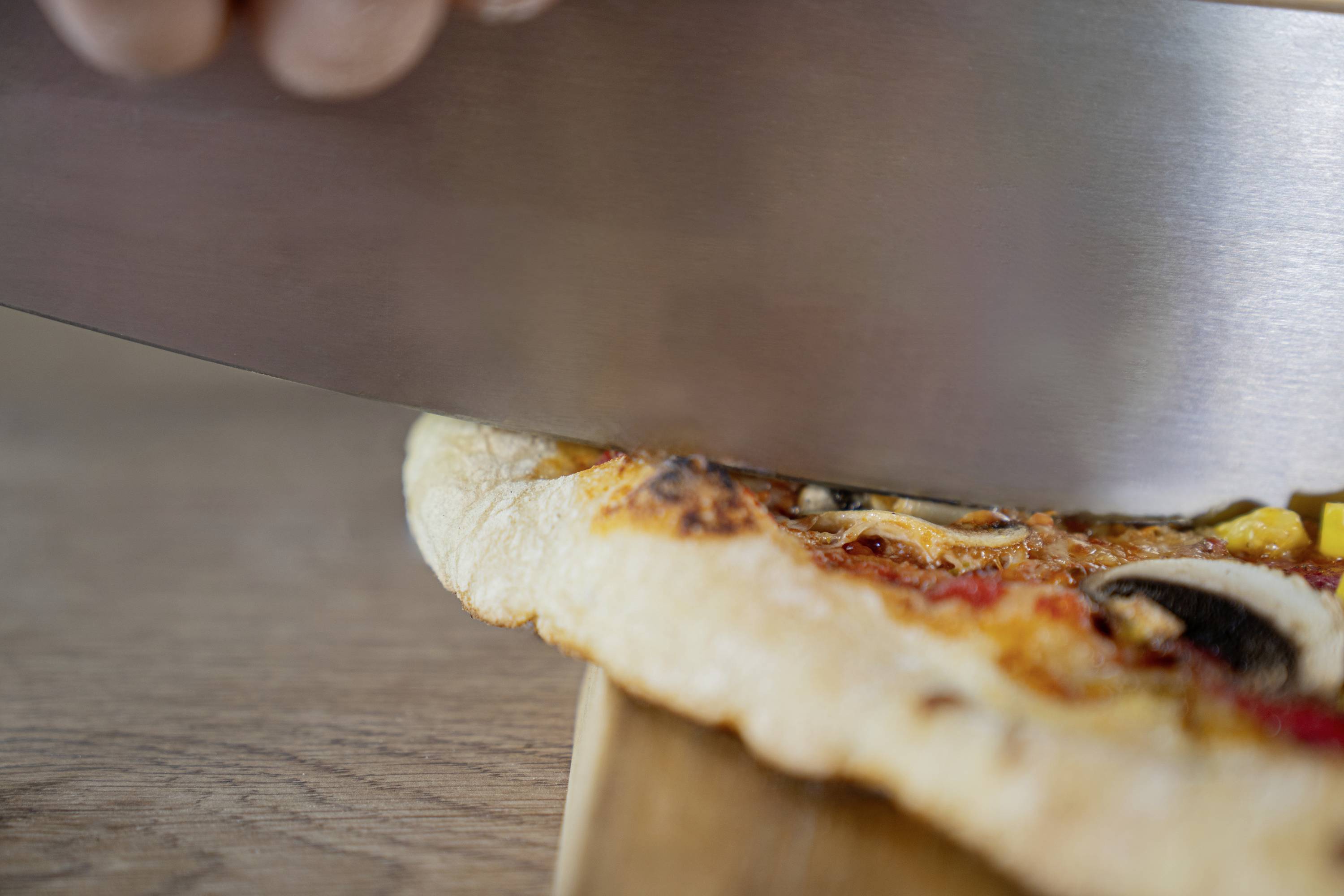 Close-up of a pizza being cut with a large knife. The pizza is topped with mushrooms and peppers.