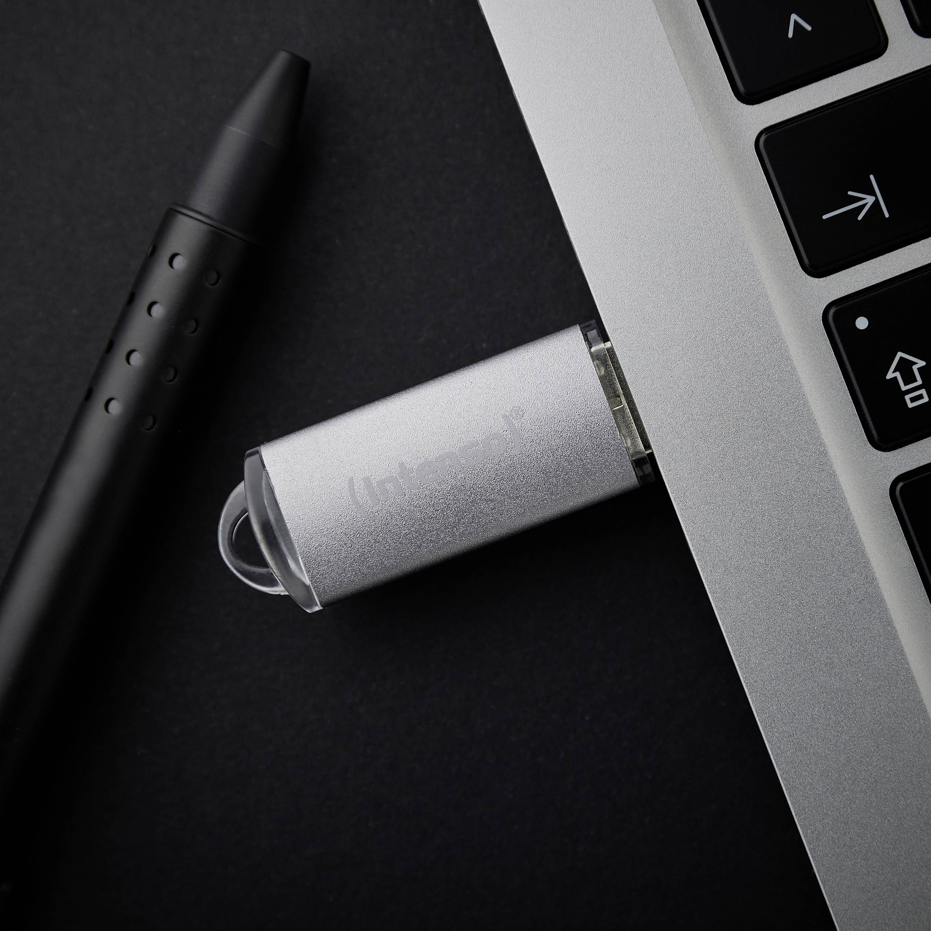 A USB drive is plugged into a laptop, with a pen lying beside it. The scene depicts a modern, professional work environment.