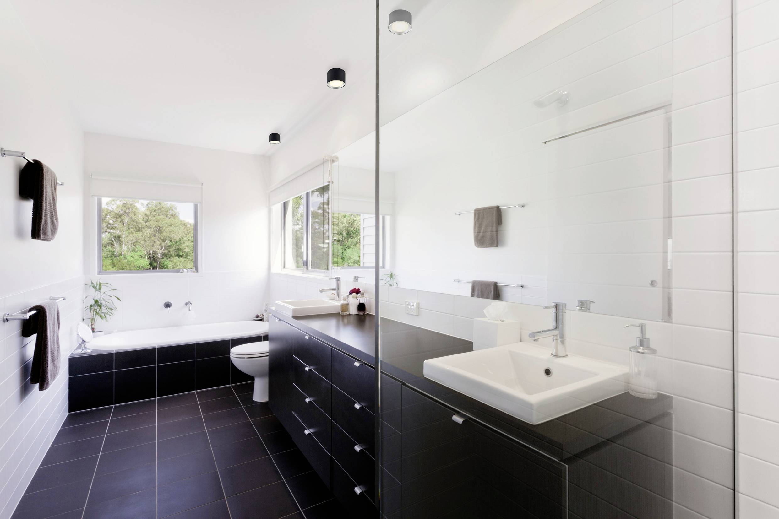 Modern bathroom with white-tiled walls, a bathtub, a washbasin on a black vanity unit, and a large mirror.