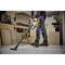 A worker is using a yellow vacuum cleaner to vacuum wood shavings in a workshop with wooden boards and shelves.