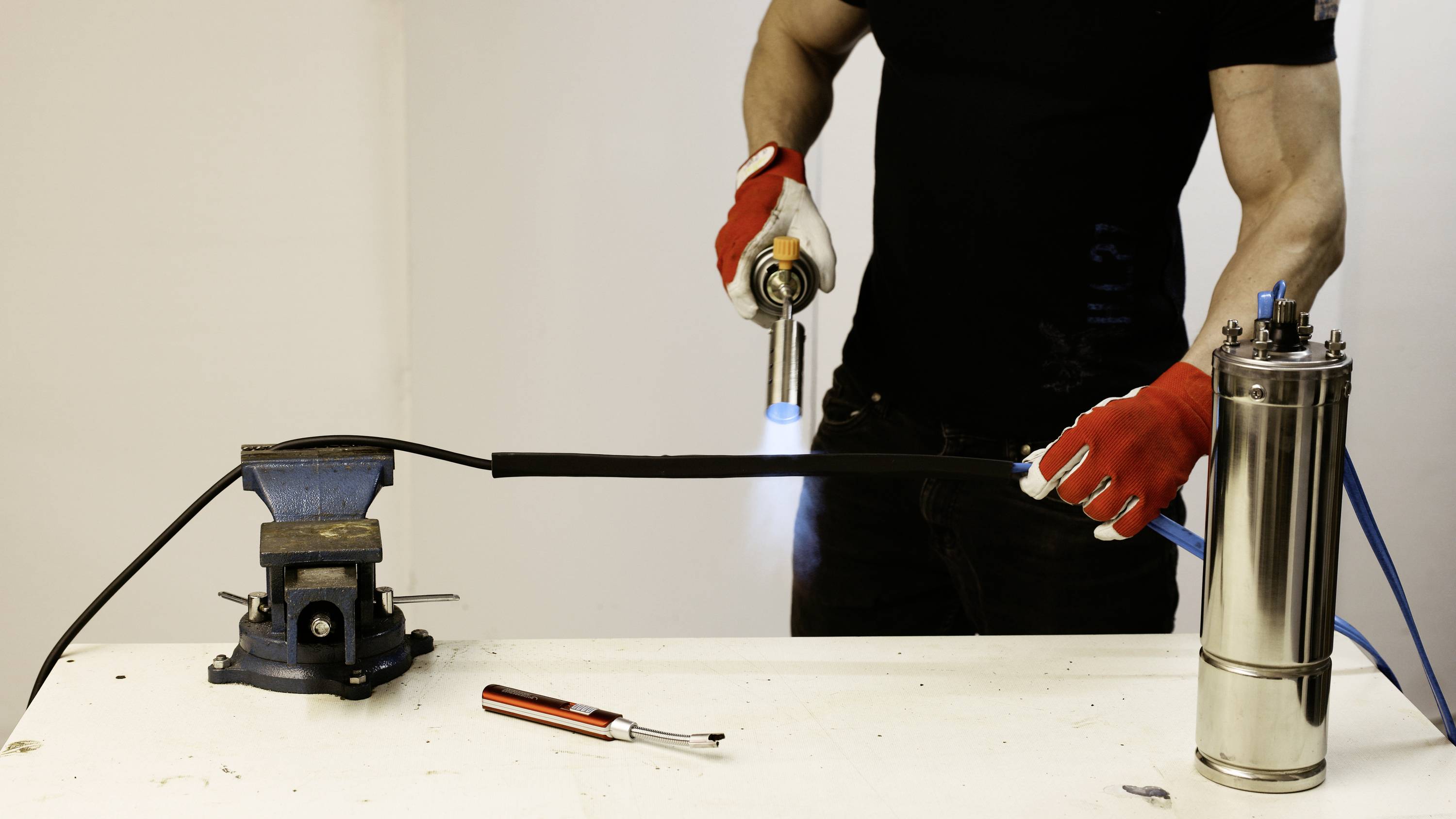 A person heats a rubber hose, which is clamped in a vice, with a flame. A tool is lying on the table.