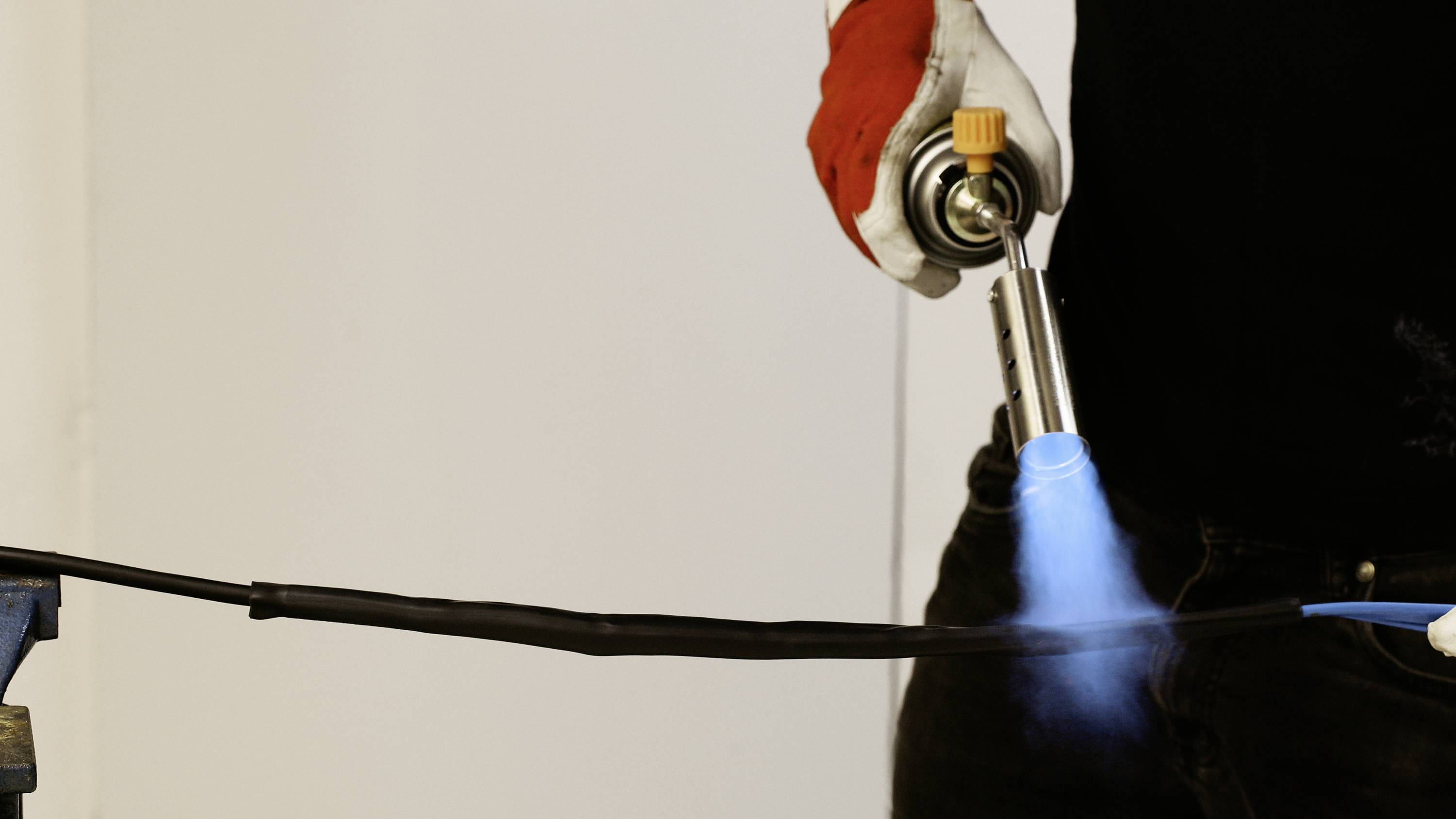 A person is heating a pipe with a blowtorch. The flame is blue. The focus is on working with the tool.