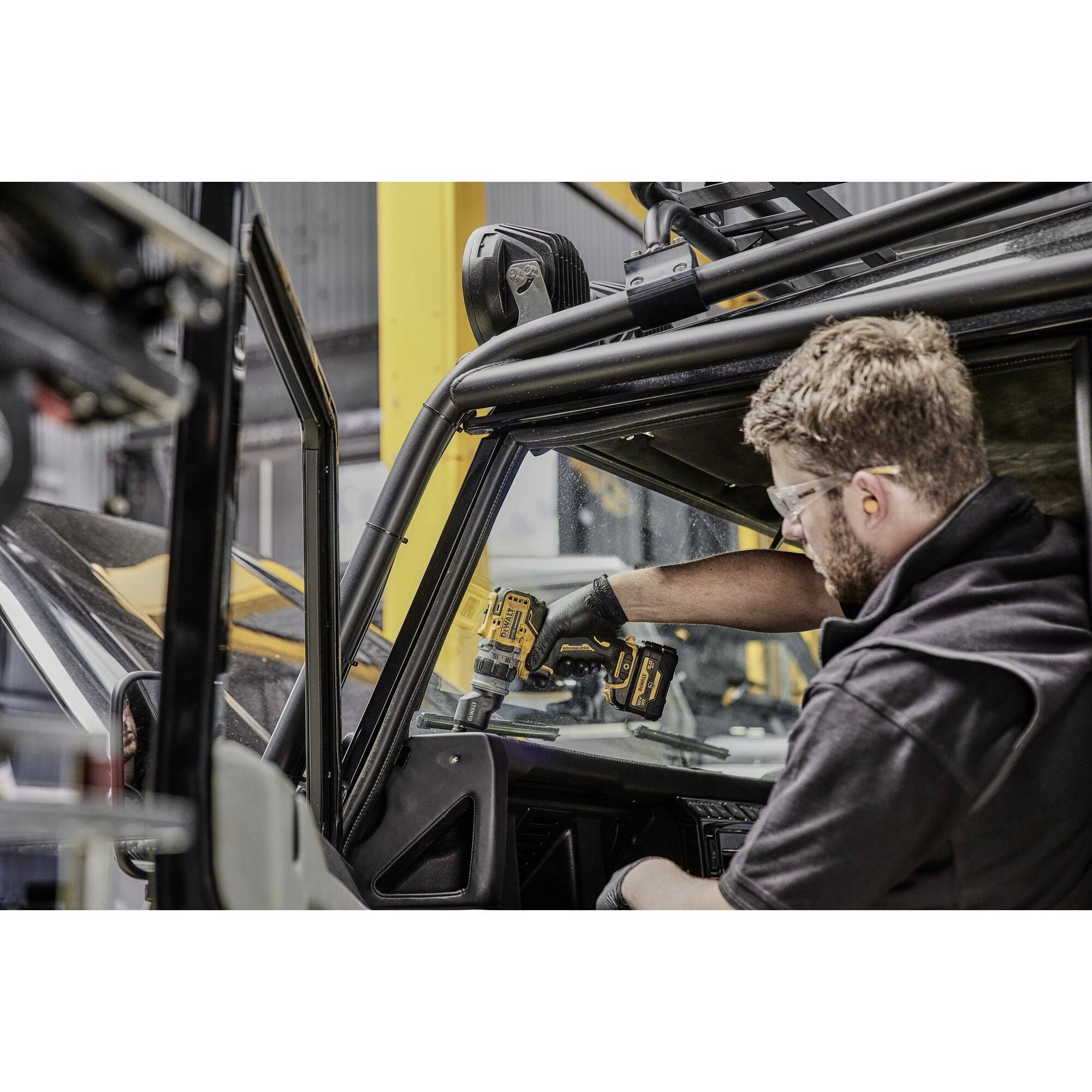 A person wearing safety glasses and gloves is working on a vehicle with an electric tool. They are securing or repairing components.