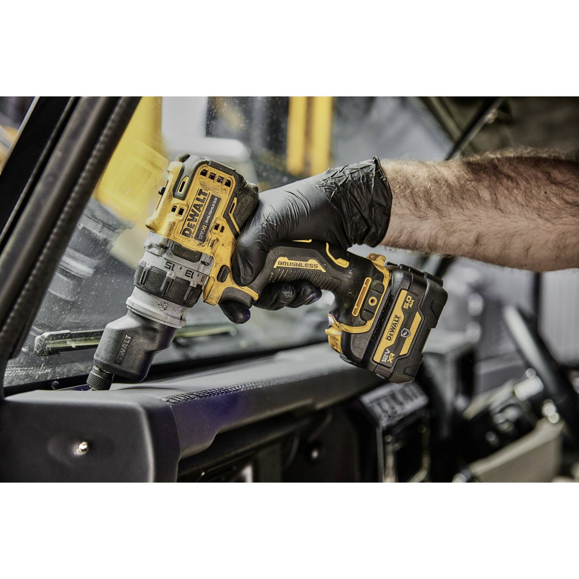 A hand wearing a black glove holds a yellow cordless drill and tightens screws inside a vehicle's interior.