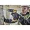 A construction worker wearing safety glasses and a hard hat is drilling a hole in a concrete wall on a building site using a cordless drill.
