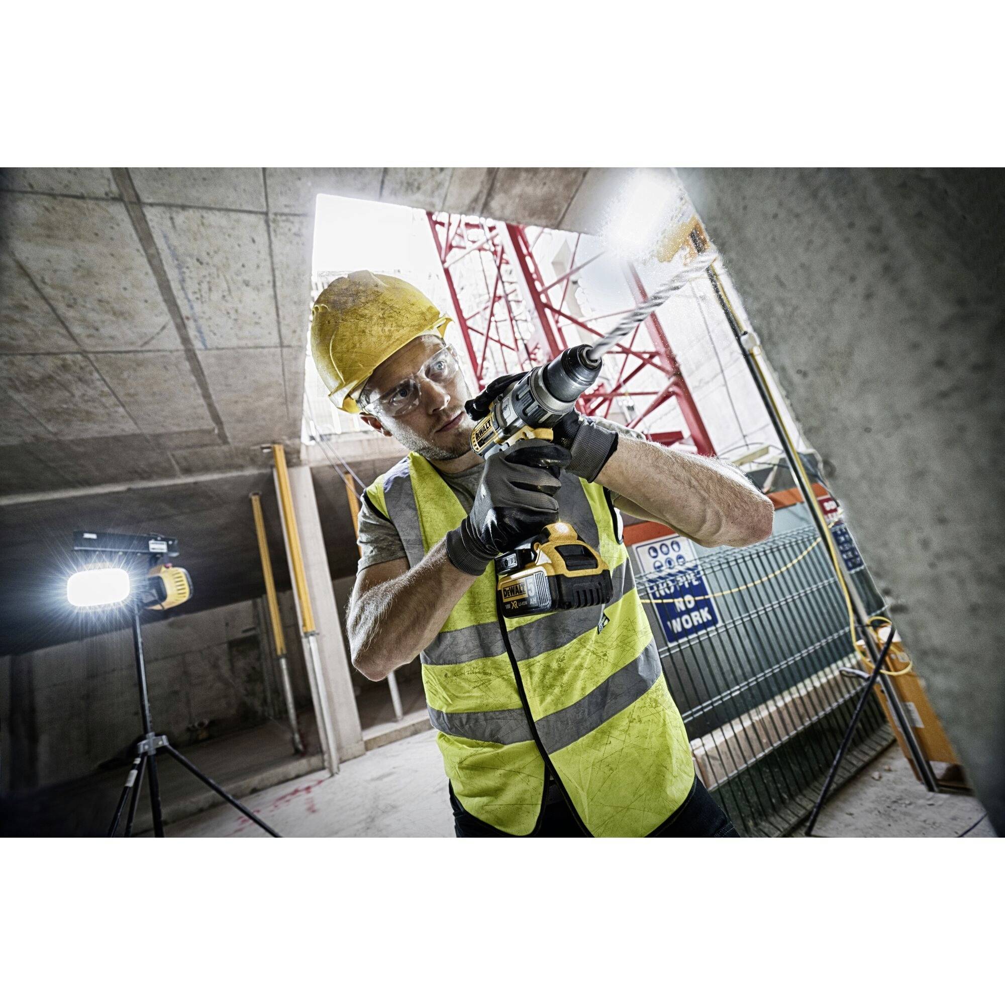 A construction worker in a yellow high-visibility vest and hard hat is drilling with an electric drill on a building site.