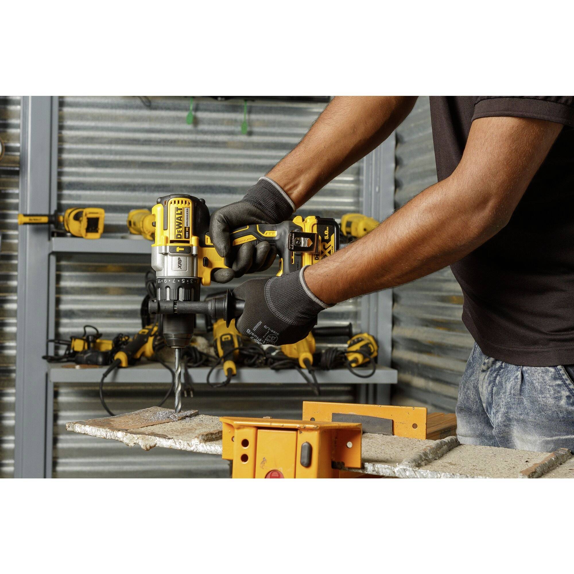 A person is using a yellow cordless drill to bore a hole in a wooden board. Other tools can be seen in the background.