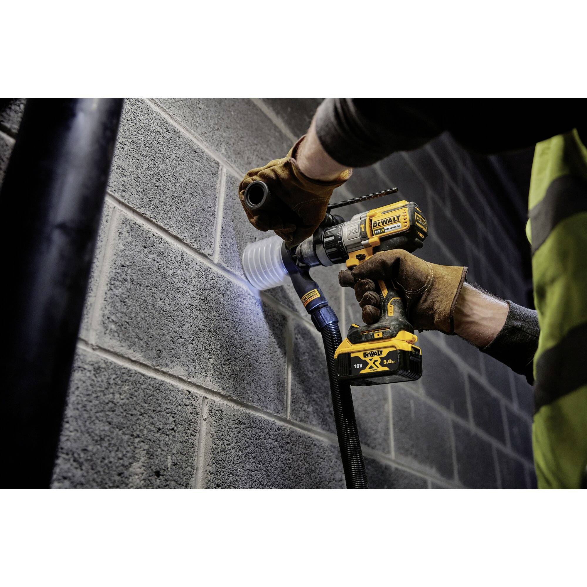 A person is drilling a hole in a grey concrete wall using an electric drill. They are wearing work clothing.