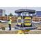 A construction worker is measuring on a building site using a surveying instrument in the foreground. The DeWalt logo is clearly visible on the device.