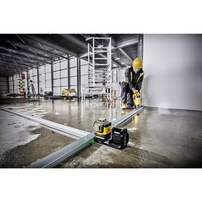 A person in workwear and a hard hat is using a laser to precisely position metal profiles on a concrete floor in a large hall.