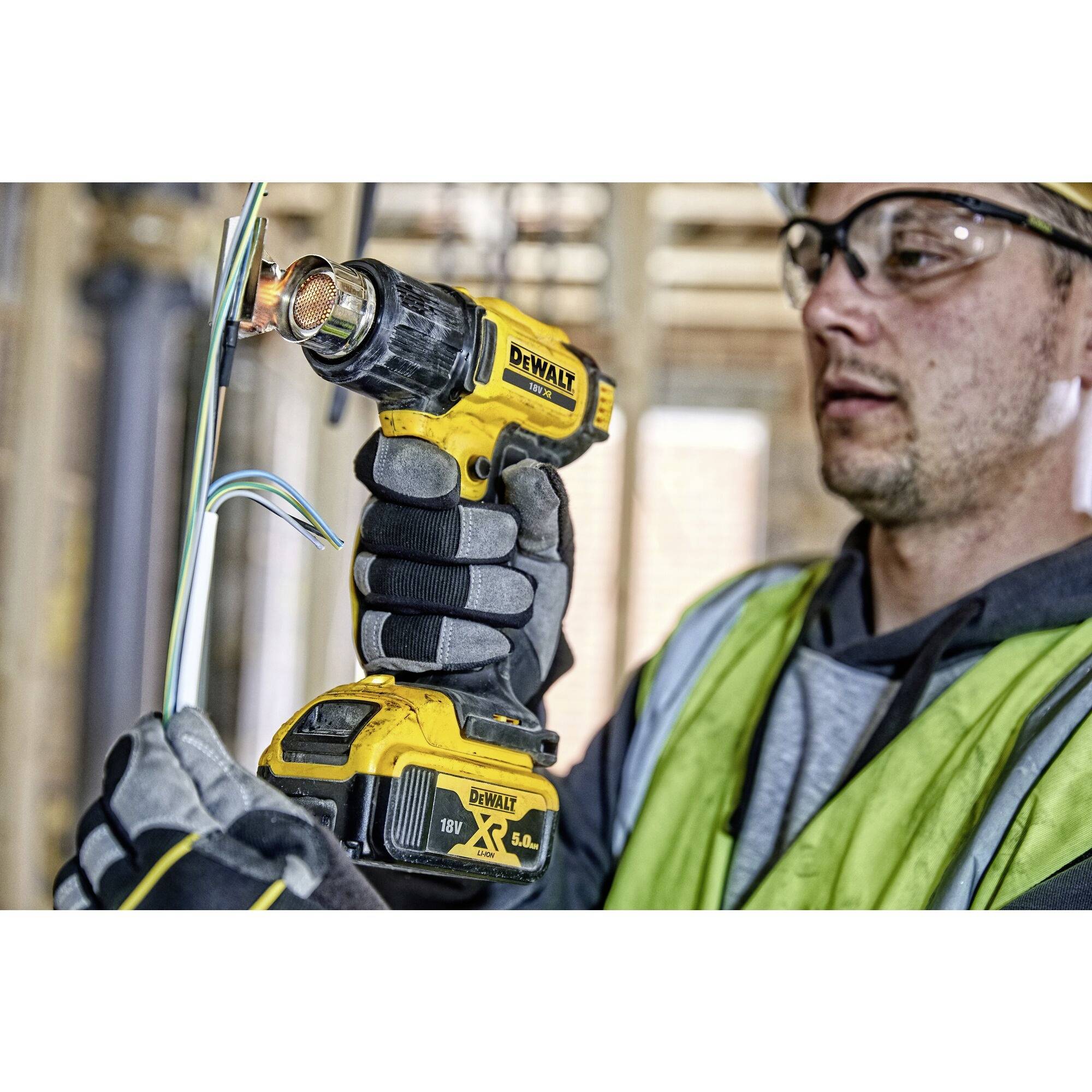 A person in safety clothing is using a yellow, cordless DeWalt tool to cut wires on a construction site.