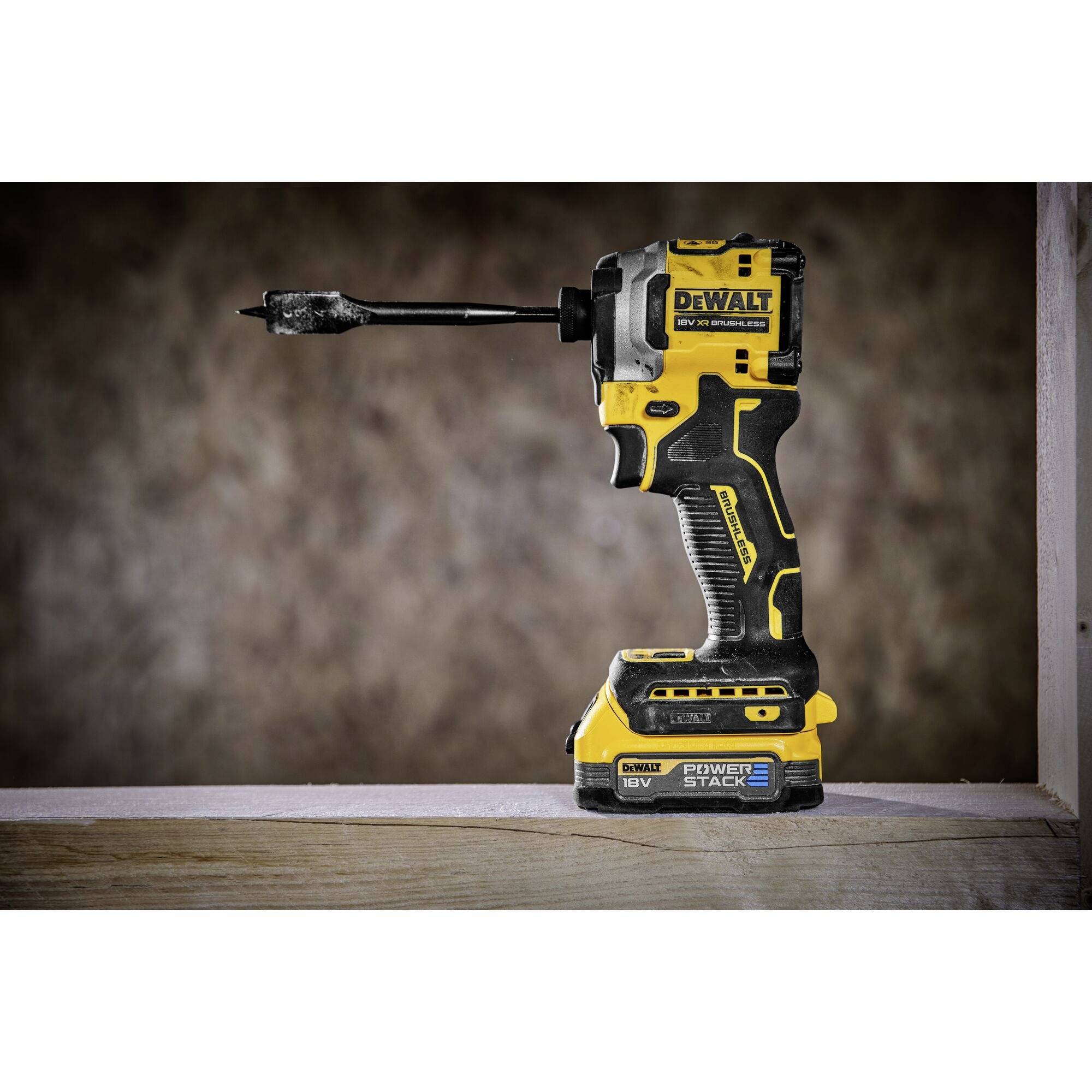 A yellow and black cordless drill stands upright on a wooden table in front of a blurred background.