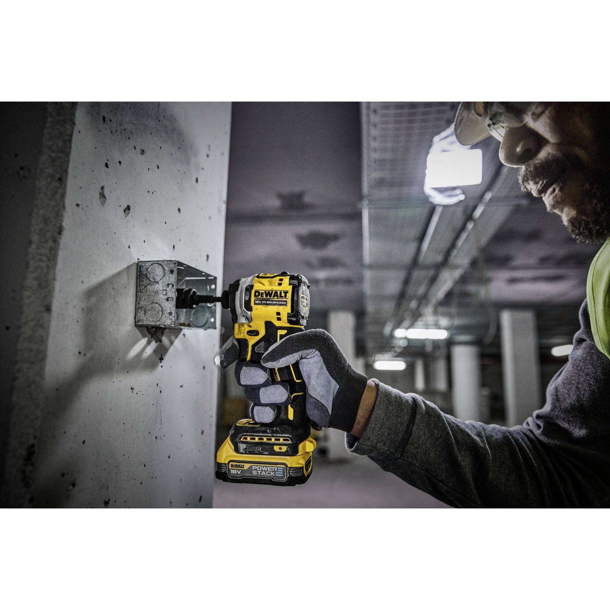 A person wearing work gloves is using a cordless drill to bore holes into a concrete wall in an industrial setting.