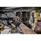 A man is repairing a vehicle with a cordless wrench. He is wearing safety glasses and gloves in a workshop.