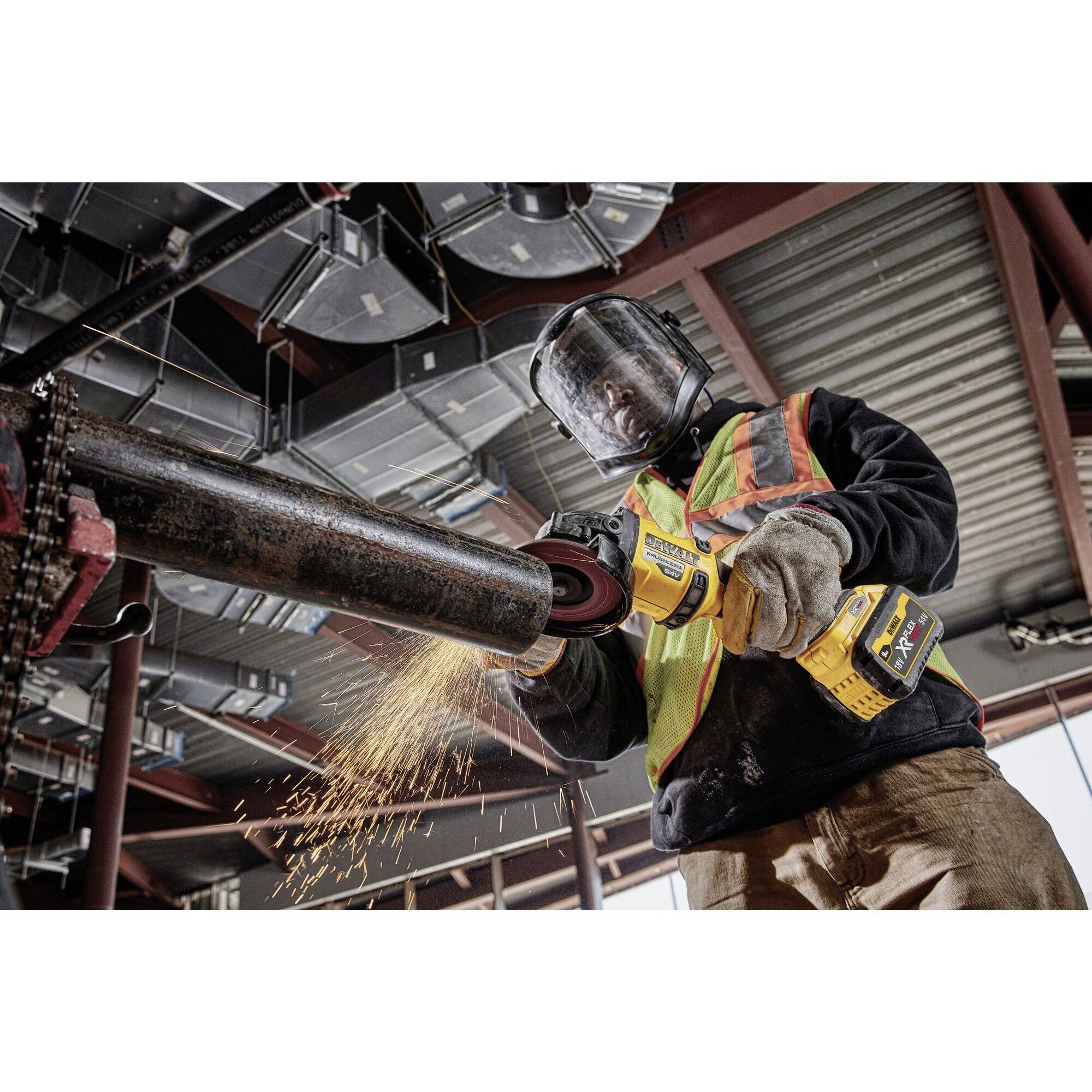 A worker in protective clothing is grinding a metal pipe with an electric grinding machine inside a construction site.