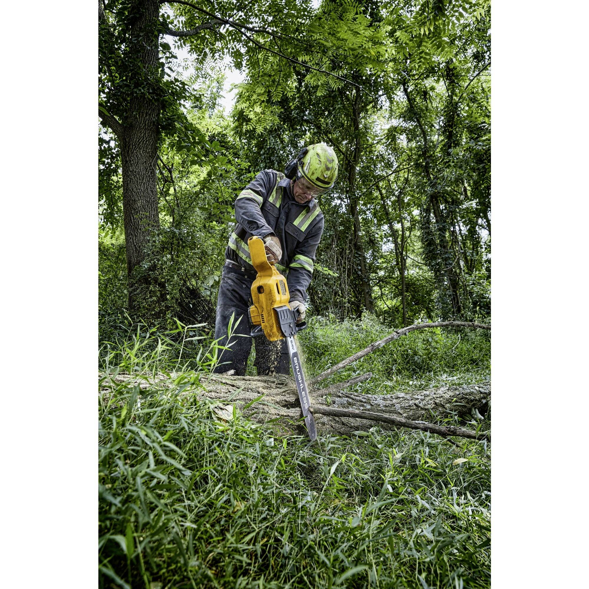 A person wearing protective equipment is cutting a tree trunk with a chainsaw in the forest.