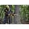 A person in protective clothing is felling a tree using a chainsaw in a wooded area. Wood chips are flying, and the tree is half-cut.