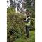 A person in safety clothing is trimming a hedge in a garden with an electric hedge trimmer.