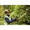 A person in safety clothing is trimming a hedge with an electric hedge trimmer in a garden.