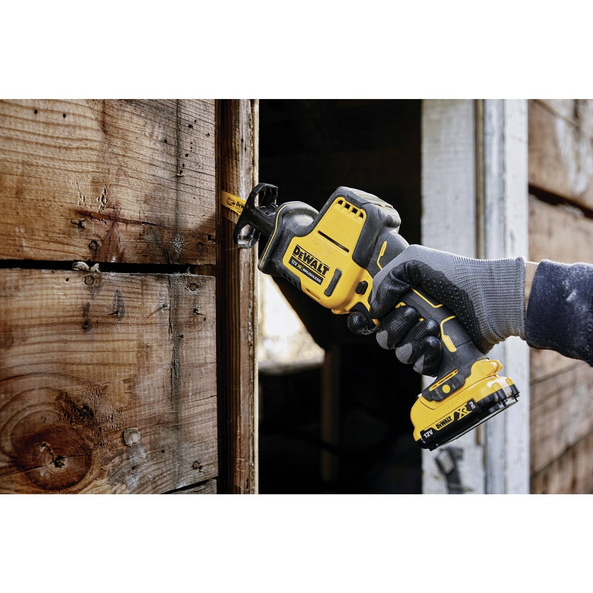 A person is sawing a wooden board with a yellow cordless saw.