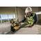 A construction worker wearing a hard hat and high-visibility vest is using an electric saw to cut wood or panels in a building with panoramic windows.